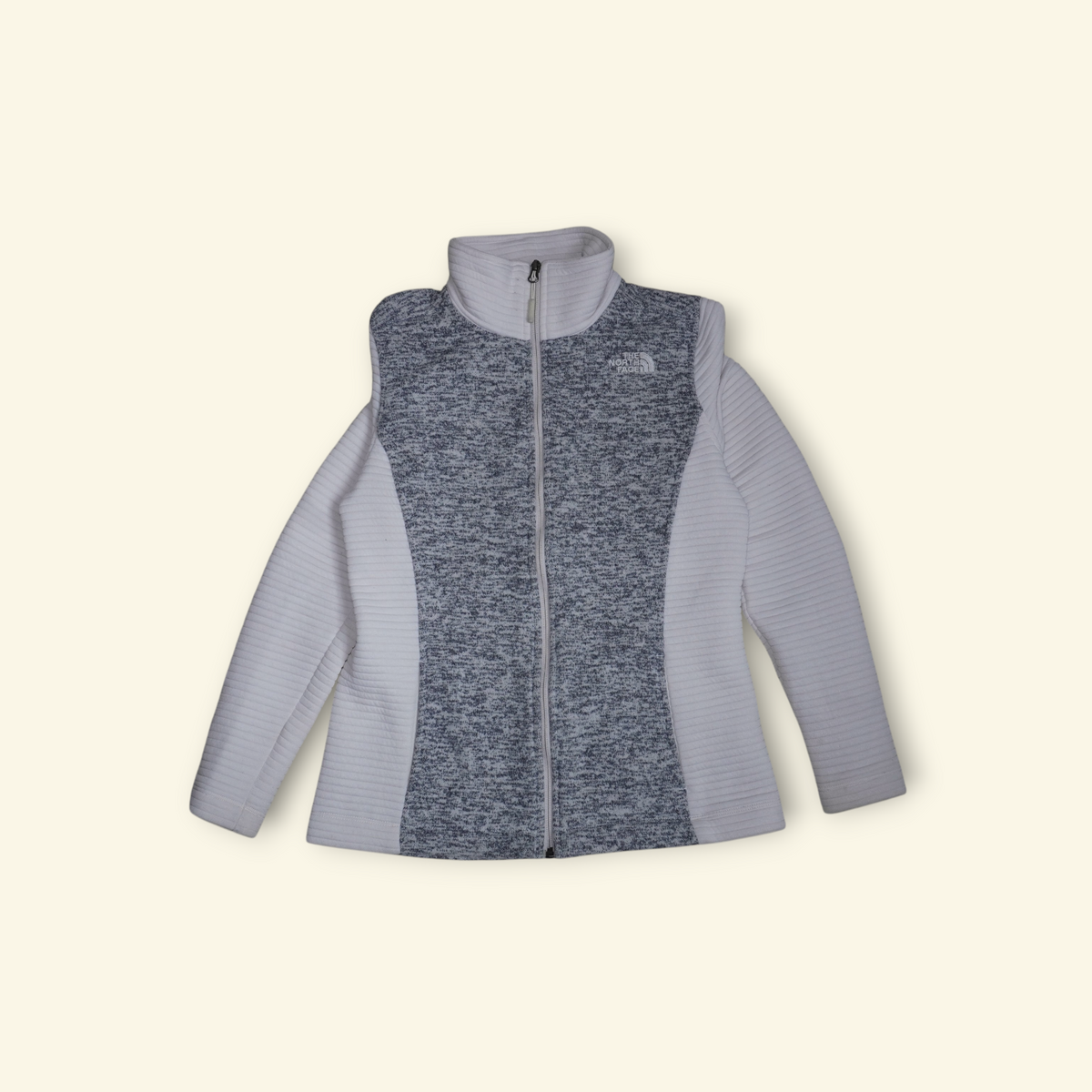 Chamarra The North Face Indi con cierre completo, diseño híbrido en gris y blanco, cuello alto y forro polar térmico.