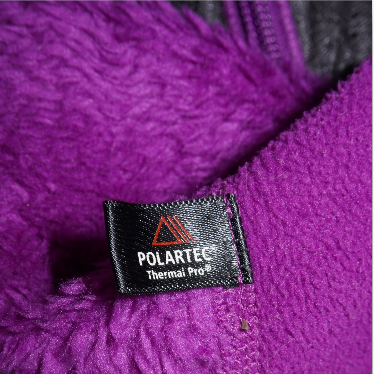 Detalle de etiqueta Polartec Thermal Pro en chamarra Patagonia morada de Mi tienda con textura de tejido técnico